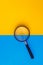 Magnifier lies on yellow and blue background. View from above. Flat lay. Copy space