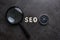 Magnifying glass, alphabet SEO and compass on dark cement background using as SEO Search engine optimization concept