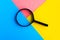 Magnifying glass on bright geometric pink, blue and yellow background.