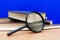 Magnifying glass a few closed books on a brown table blue background