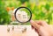 A magnifying glass looks at a wooden house in a trading cart on nature background. The concept of buying and selling real estate