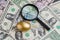 Magnifying glass with shiny golden egg under pile of US America dollar banknotes money metaphor of precious wealth, finding good