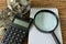 magnifying glass on white paper and calculator with stack of coins on wood table as financial saving or tax concept