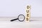 magnifying glass and wooden blocks with text DUES on wood table, grey background