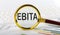 Magnifying glass with the word EBITA on chart background