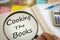 Magnifying glass writing `Cooking the books` in a notebook.  Creative accounting concept.  Calculator, office accessories, clock