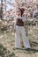 Magnolia park woman. Stylish woman in a hat stands near the magnolia bush in the park. Dressed in white corset pants and