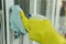 Maid wearing yellow protective gloves cleaning door entrance with rag and detergent spray bottle