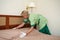 Maid woman, dressed in green, putting blanket on bed