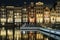 The main street of Damrak Amsterdam the netherlands with dancing houses and reflection in the water at night