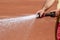 Maintenance of clay tennis court. Water jet and spray from a hose on a blurry orange background. Close up. Copy space