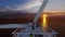 Maintenance worker on top of a offshore wind turbine with oil rigs against sunset