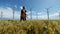 Maintenance workers in a wheat field with wind turbines in the distance, 4K