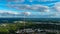 A majestic aerial shot of miles of green trees with buildings nestled within the trees with a red and white communication tower