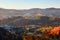 Majestic autumn rural scenery. Landscape with mountains, fields and forests. There are trees on the lawn full of orange leaves.