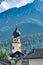 Majestic bell tower stands tall against the backdrop of a stunning mountain range in San Candido
