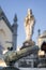 Majestic marble statue atop a pedestal with a knocker of a grave in the foreground