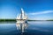 majestic sailboat gliding through calm waters, with clear blue skies and greenery in the background