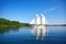 majestic sailboat gliding through calm waters, with clear blue skies and greenery in the background