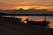 Majestic sunset on sea - golden sky, last sunbeams, dark volcano, black silhouette of fishing boat and walking people on beach.