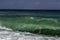 Majestic Turquoise and deep green swell crashing into a beach on a blue sky summer day in Sicily