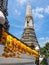 The majestic Wat Arun Temple in Bangkok, Thailand, with yellow flowers (Phuang Malai) in the foreground and a blue sky