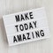 `Make today amazing` words on a lightbox on a white wooden background. From above, overhead, flat lay, top view. Close-up