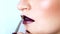 Make-up artist is applying bright purple tinsels on model\'s lips with a brush. Her mouth is slightly open. Close up.