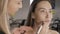 make up artist doing makeup for brunette asian woman with brush in beauty salon