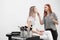 Make-up artist redhead girl makes makeup beautiful blonde woman model on white background. Next to the cart with tools