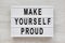 `Make yourself proud` words on a lightbox on a white wooden background, top view. Flat lay, overhead, from above. Close-up