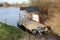 Makeshift homemade river barge made of metal barrels and wooden boards with two small benches parked in narrow canal and tied to