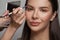 Makeup artist applies brown color shadow to a eyebrow of brunette woman. Make-up concept
