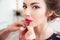 Makeup artist applying pink lipstick to lips of woman