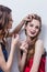 Makeup artist paints the eyebrow of a beautiful girl, blonde, brown eyeliner, she grins and holds her hand on the makeup, white ba