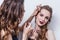 Makeup artist paints the eyebrow of a beautiful girl, blonde, brown eyeliner, she grins and holds her hand on the makeup, white ba