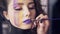 Makeup artist uses brush to apply lipstick to model`s lips. Model with false lashes and face art painting preparing to