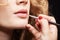 Makeup artist visagiste using brush for application lipstick on lips of young caucasian model with wavy ginger hair