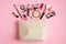 Makeup bag with cosmetic products spilling out on to pastel pink background. Flat lay, top view. Glamour make up artist pouch with