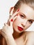 Makeup products. Young beautiful girl with gold earrings and ring smiling on white background. Red nails with manicure