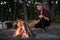 Making campfire at a forest. Going into the wild concept: camping place with vintage backpack, thermos and male in casual clothes