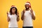 Making Christmas wish. Young african american couple in santa hats crossing fingers for luck over yellow background