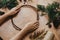 Making christmas wreath. Hands holding wooden circle and fir branches, pine cones, thread, scissors, herbs on wooden table.