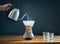 Making coffee by an alternative method, pouring hot water from a kettle into a glass decanter on wooden table