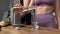 Making green juice at home: female hands pouring water into a glass in the kitchen. Unrecognizable fitness woman in