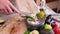 Making guacamole sauce - woman pouring chopped garlic into bowl with mashed avocado and onion