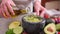 Making guacamole sauce - woman pouring olive oil into mixed ingredients in marble bowl mortar