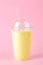 Making a milkshake. plastic disposable glass with a banana milkshake on a bright trendy pink background
