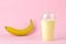 Making a milkshake. a plastic disposable glass with a banana milkshake and a fresh banana on a bright trendy pink background