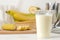 Making a milkshake. plastic disposable glass with a banana milkshake, ingredients for cooking and mixer on a light background
